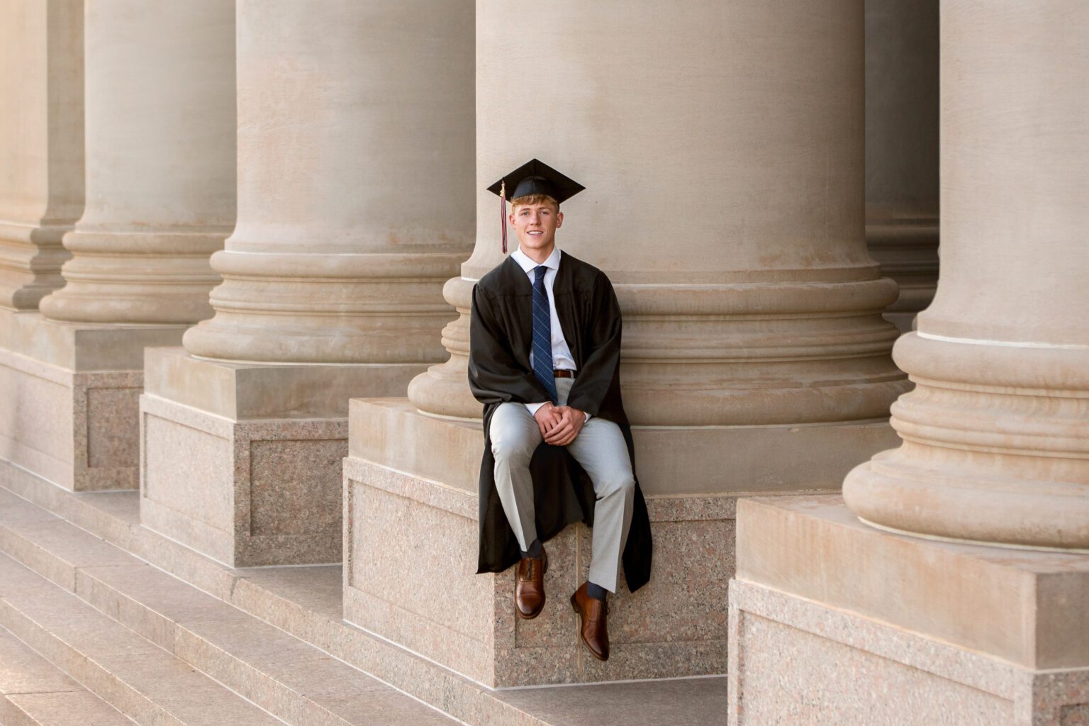 This photo is a senior guy in a cap and gown at the state capitol, showing off senior photography trends