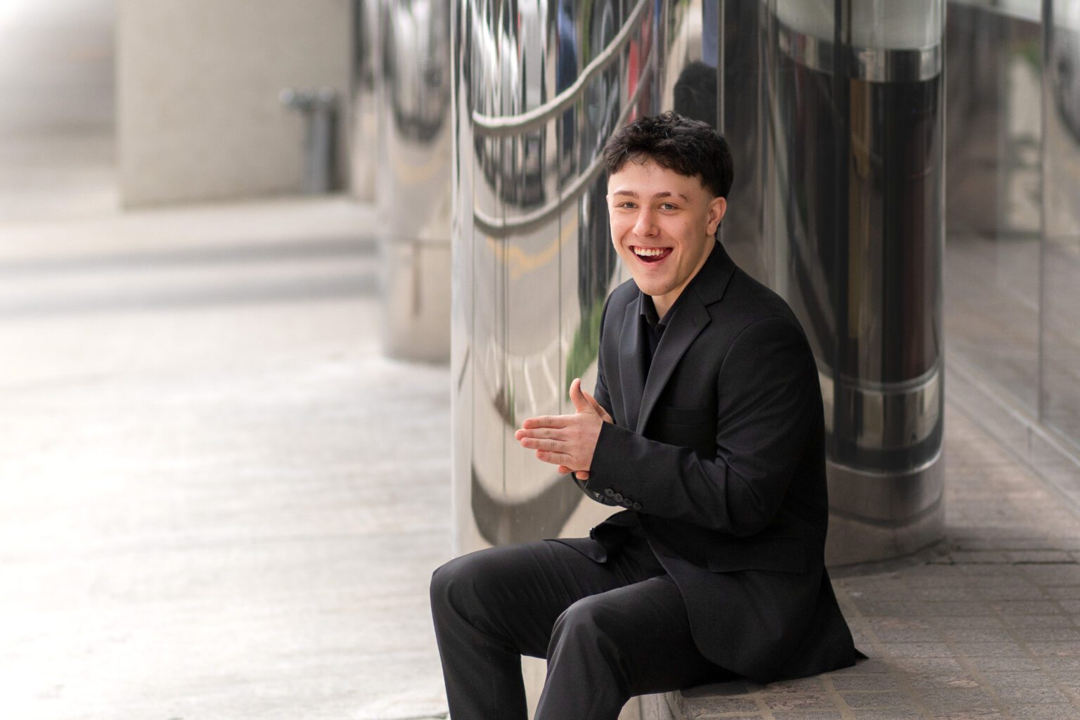 senior boy posing in a suit and sitting down in Oklahoma City Leadership Square for Missy Mayo Photography