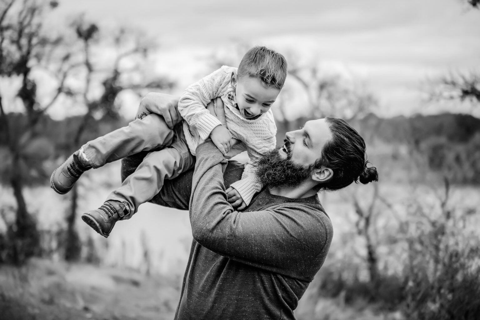 dad lifting toddler in the air laughing during outdoor family photo session with Oklahoma City family photographer